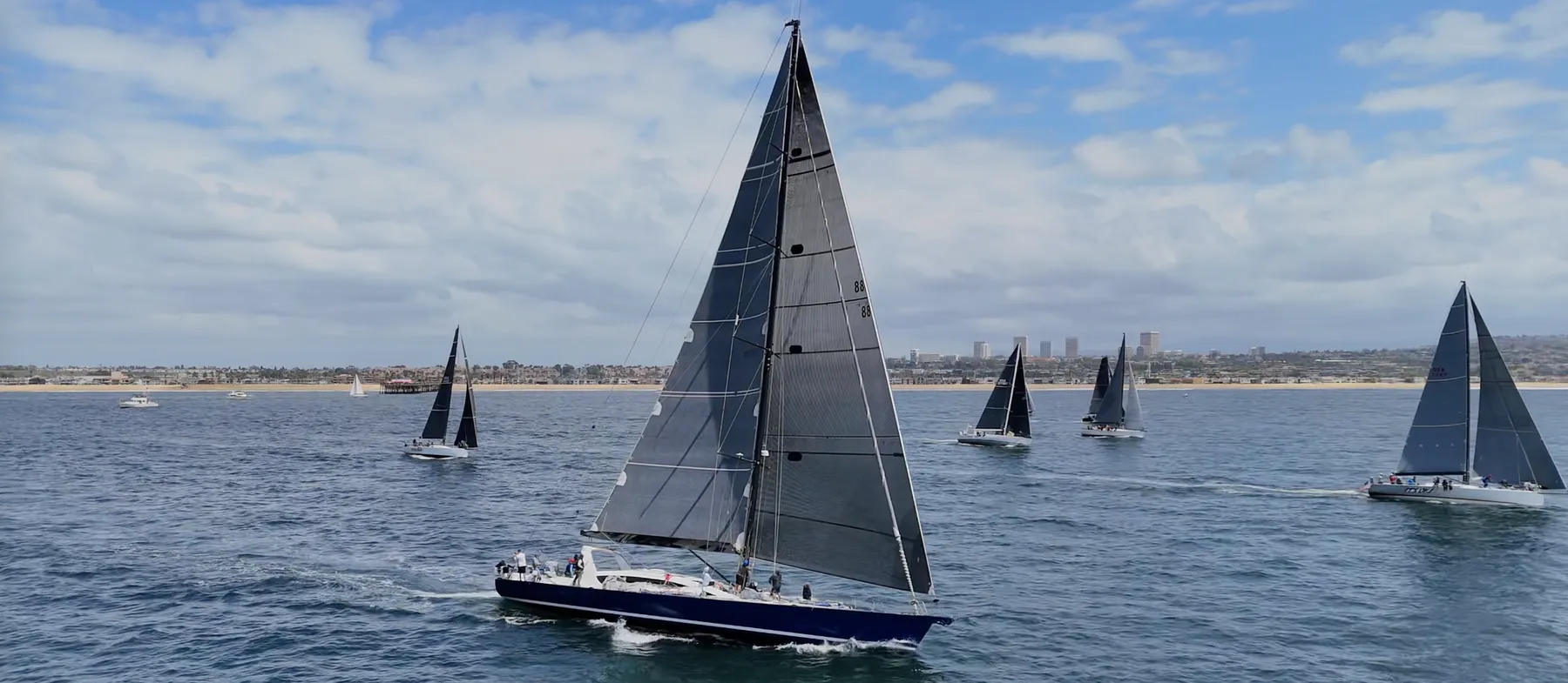 Aerial view of a sailboat regatta — the fleet heeled over under sail on blue water off the coast.